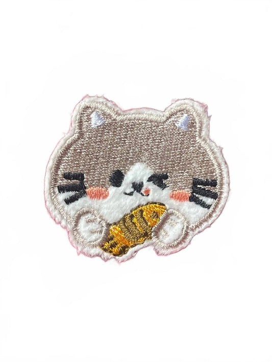 Embroidered patch of a cat holding a fish on a white background