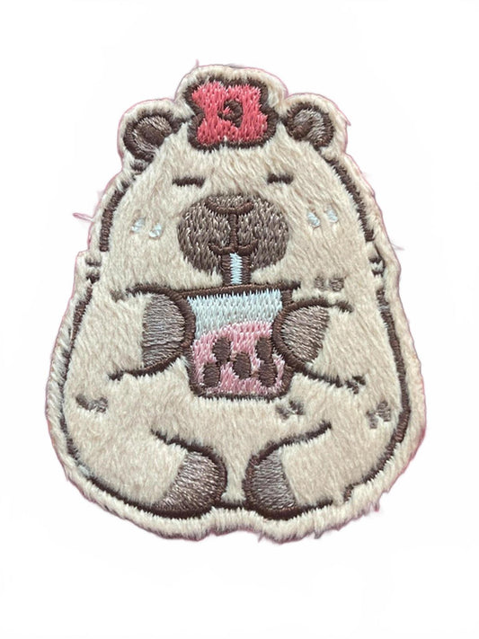 Embroidered patch of a capybara with a pink bow on a white background